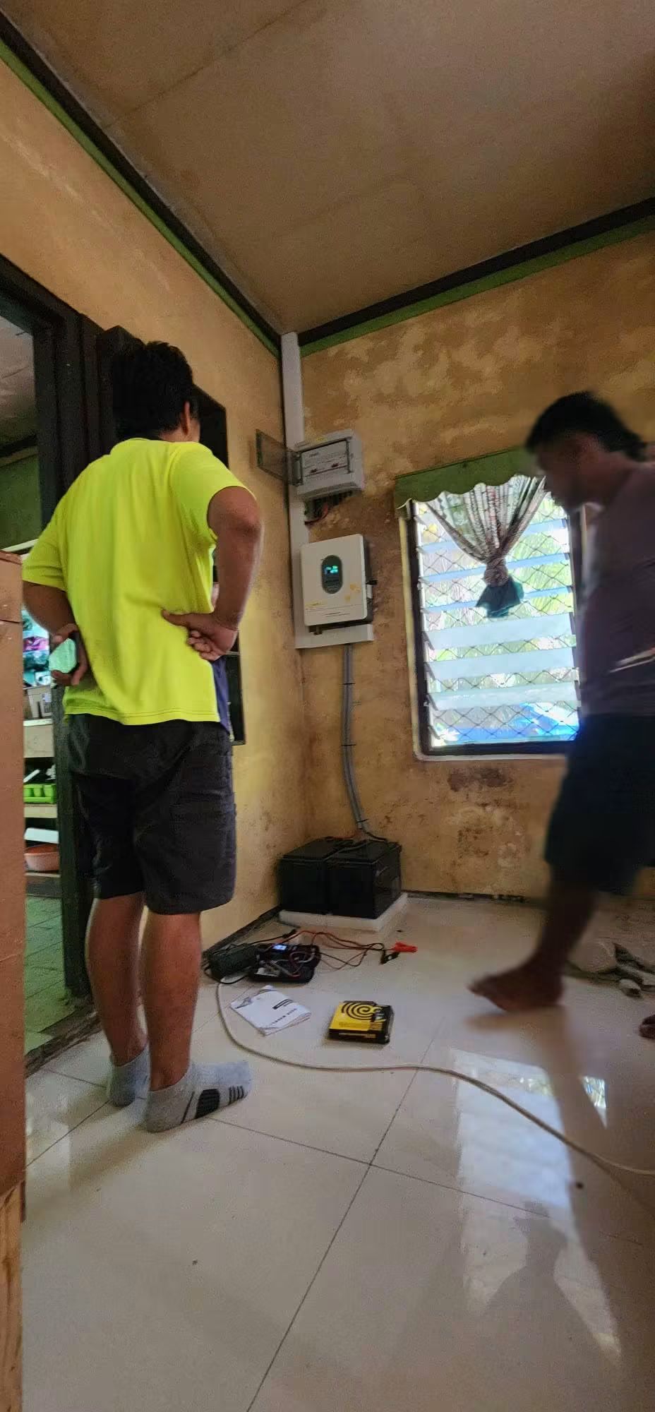 Interior view of an installed solar inverter and battery with people nearby