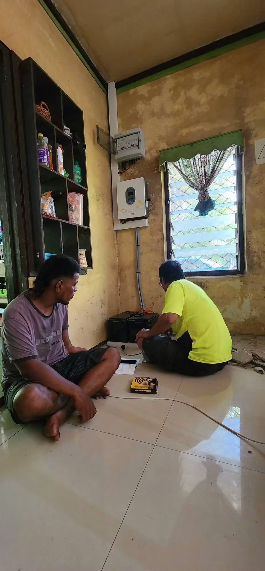 Two people working beside a battery and installed inverter